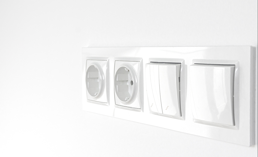Weiße Durchgangsschalter und Steckdosen aus Kunststoff an einer weißen Wand